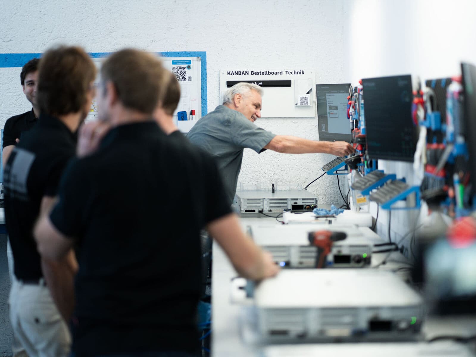 Besuchergruppe einer Lean-Tour in der Tradeo-Technik: ein Kollege zeigt auf die Werkzeugwand neben dem KANBAN-Bestellboard